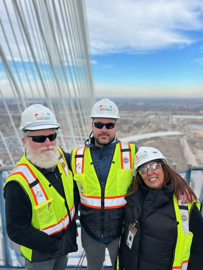 Justin on a high-rise construction site with two colleagues in hard hats and hi-vis vests