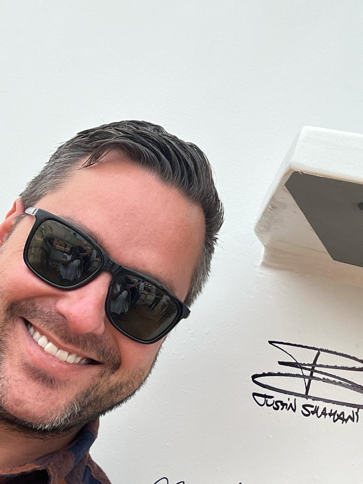 Justin smiling beside his signature written on a wall